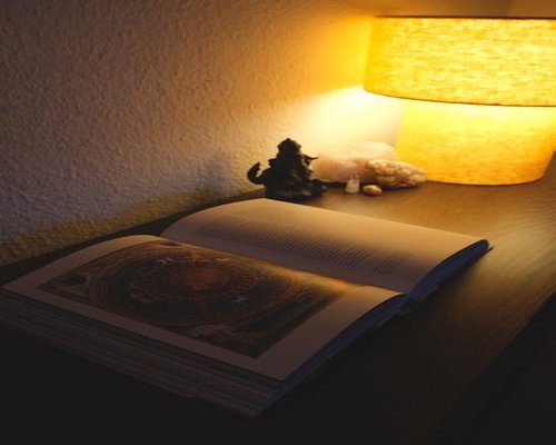 A cozy bedroom corner with a reading lamp illuminating an open book, accompanied by soft background room lighting